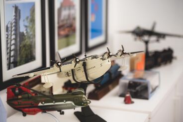 Close-up of model airplanes displayed on a shelf with framed pictures in the background