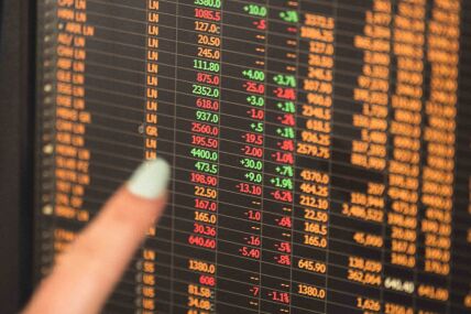 Close-up of a financial data screen displaying stock prices with a hand pointing at one of the rows